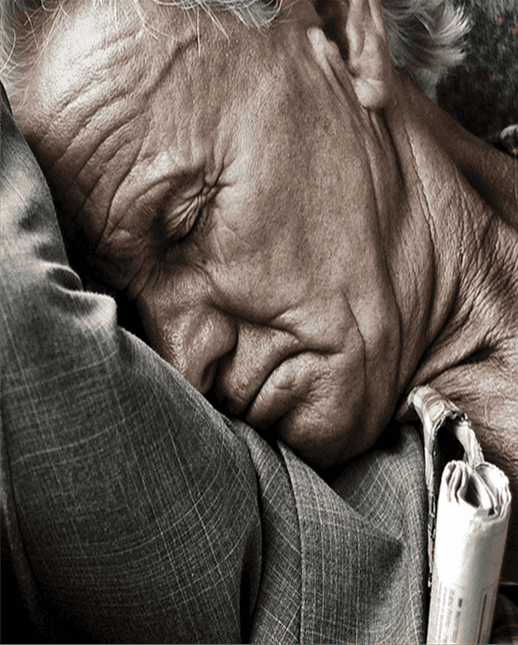 Older gentleman sleeping with his arm up and head resting against it.