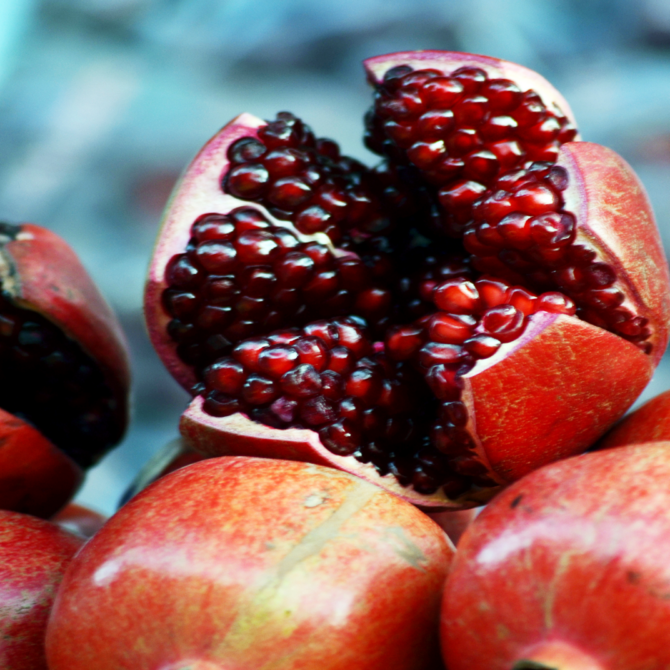 An open pomegranate is on top of pile of unopened pomegranate.